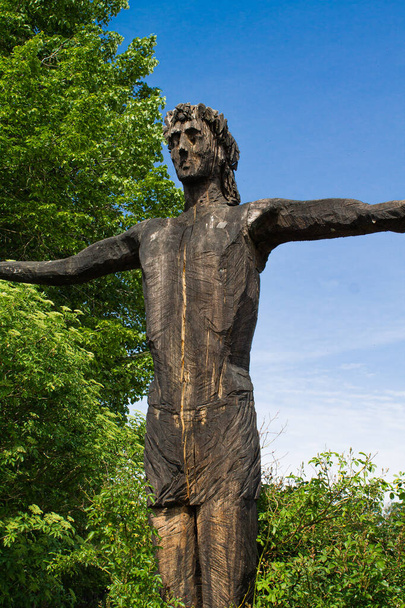 大きな木と青い空の前に広がった腕を持つ完全なポーズで立っているイエスの木像の側面図 - 写真・画像