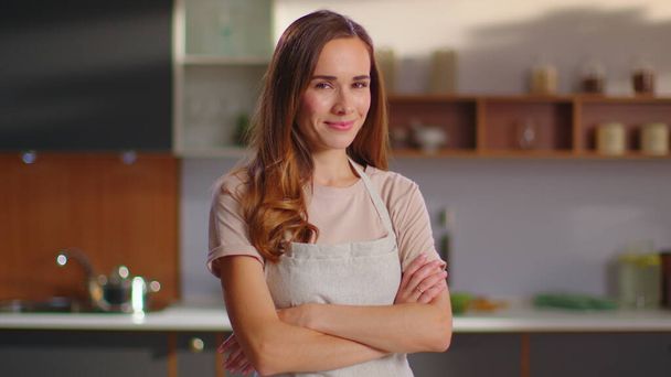 Kobieta z skrzyżowanymi rękami stojąca na kuchni. Kobieta w fartuchu kuchennym w domu - Zdjęcie, obraz
