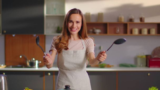 Žena držící lžíce v rukou na kuchyni. Žena se dívá na kameru v kuchyni - Fotografie, Obrázek