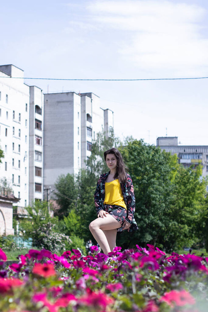 Mulher morena jovem atraente em camiseta amarela e traje de shorts floridos. perto de um arbusto de flores. espaço de cópia
. - Foto, Imagem