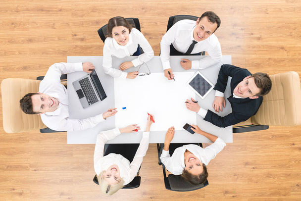 Les gens d'affaires heureux travaillent avec une feuille blanche sur la table. vue d'en haut
 - Photo, image