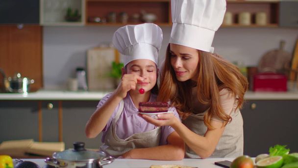 Mother and daughter in hats decorating cake with cherry on domestic kitchen - Foto, Bild