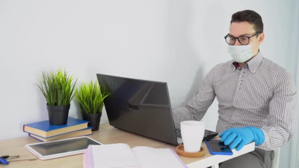 Bělošský zaměstnanec nosí šedou kostkovanou košili, kalhoty, černé brýle, ochrannou masku, modré rukavice, vstaňte od stolu s notebookem, šálkem, knihami, telefonem. Muž opouští pracoviště. Konec pracovního dne. - Záběry, video