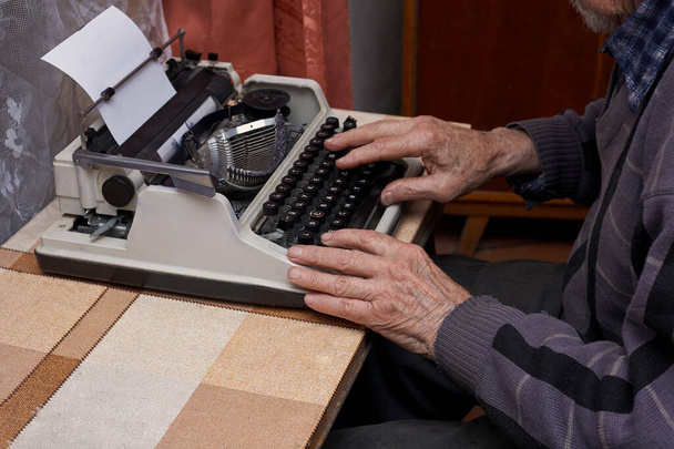 Ένας συνταξιούχος δακτυλογραφεί. Η γραφομηχανή είναι παλιά. Οριζόντια πλαίσια. - Φωτογραφία, εικόνα