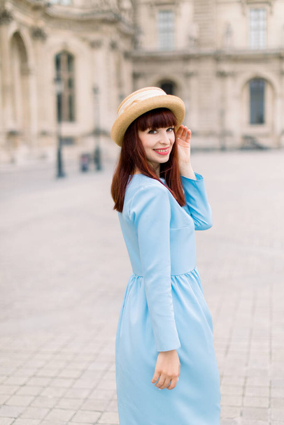 Portrait of pretty smiling young woman, wearing elegant blue dress posing looking at camera, while standing on the territory of vintage ancient buildings - Foto, afbeelding