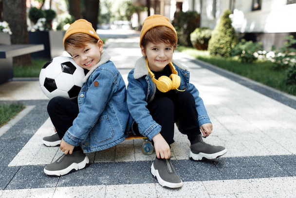 Two cute twin boys with happy faces sitting on the skateboard or pennyboard in the street. - Photo, Image
