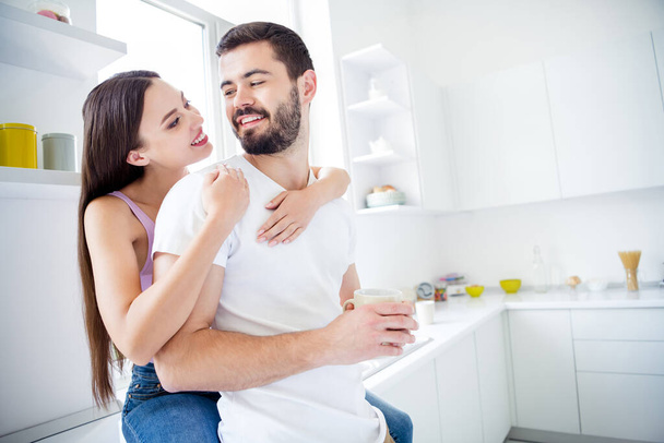 Photo of two people man woman hug embrace piggyback have rest relax weekend man hold mug beverage coffee latte girl sit window sill in kitchen house indoors - Foto, afbeelding