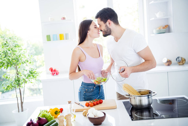 Photo of two people passionate tender gentle spouses prepare valentine day date dish nutrition woman hold bowl salad man boil macaroni kiss romance in kitchen house indoors - Photo, Image