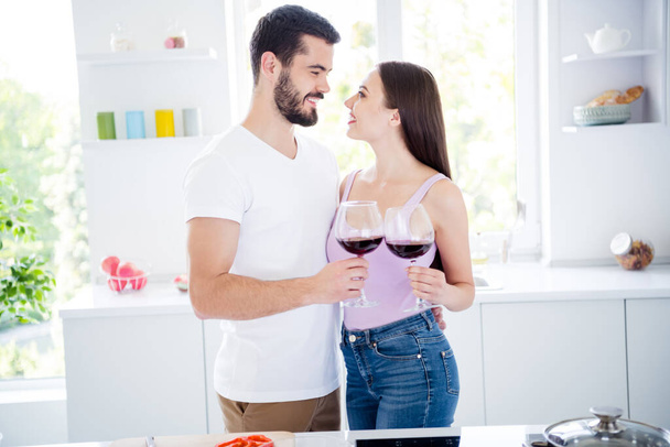 Profile side photo of two people married bonding spouses have passionate date evening dinner meal hold wine glass cheers toast clink woman man hug embrace tender in house kitchen indoors - Foto, Imagen
