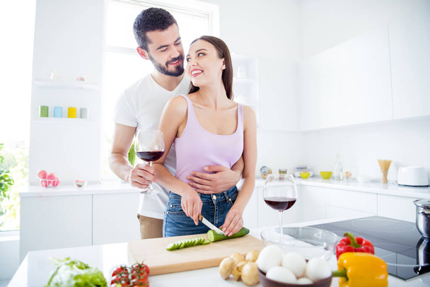 Portrait of affectionate passionate two people man hold glass wine hug woman cut knife fresh organic cucumber enjoy 14-february dinner dish stay home quarantine in house indoors - Foto, imagen