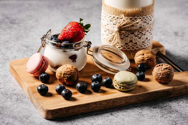 Stillleben eines Snacks bestehend aus Blaubeerjoghurt, Walnüssen, Erdbeere und Milch in einer Flasche, die von Hand mit Seil und Spitze dekoriert ist - Foto, Bild
