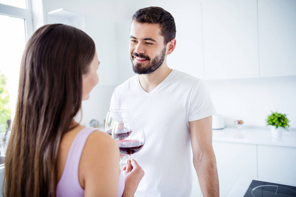 Back rear spine view photo of positive bonding spouses man woman have stay home romantic meal hold glass wine toast clink cheers in kitchen indoors - Foto, Imagem