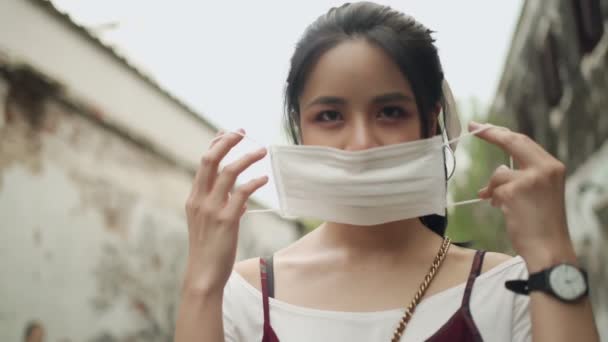 Aantrekkelijke schone huid aziatische vrouw met wit beschermend masker tijdens het omdraaien, covid-19 corona preventie, bomen achtergrond, Dag natuurlijk licht, nieuwe normale, outdoor scene - Video