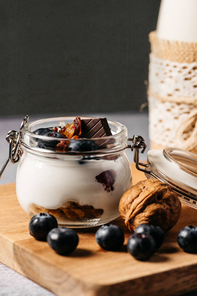 Bodegón de un snack compuesto por yogur de arándano, nueces, chocolate y leche en una botella decorada a mano con cuerda y encaje
 - Foto, Imagen