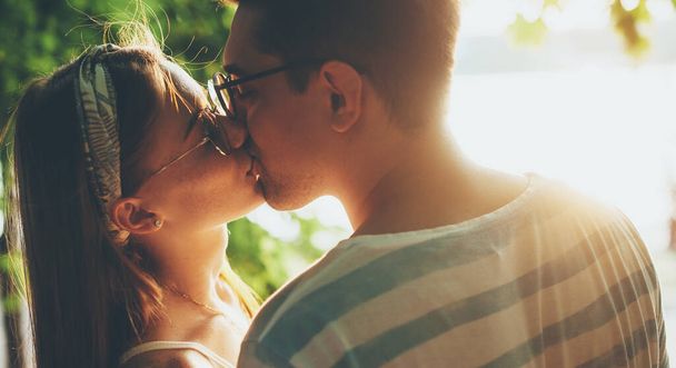 Charming couple wearing eyeglasses and kissing outside in the light of fun in a park - Photo, Image