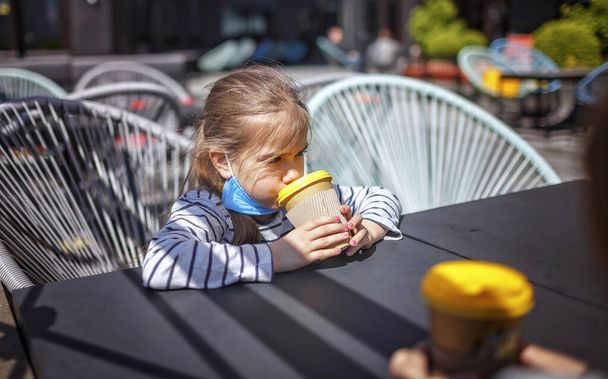 New normal reality, stay safe in street cafe, kids with protective medical mask holding paper cups and waiting for breakfast at open terrace of restaurant, outdoor family food - Photo, Image