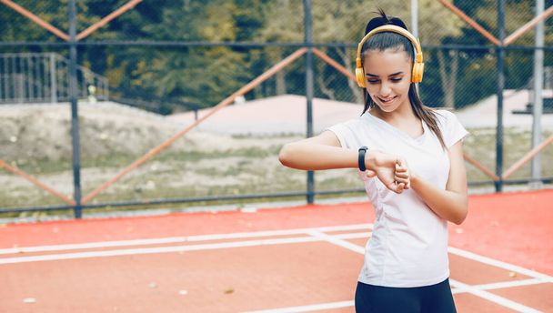 Brunette fille caucasienne fixer le temps sur ses montres intelligentes après avoir fait des exercices du matin à l'aide d'écouteurs
 - Photo, image