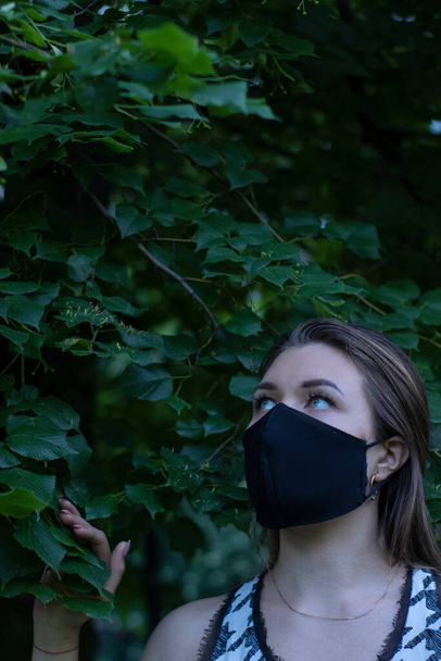Mulher loira muito jovem com máscara facial preta médica. em um arbusto, floresta. conceito covid-19. realidade moderna. espaço de cópia
. - Foto, Imagem