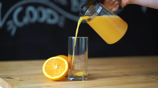 versando il succo d'arancia da un decanter in un vetro trasparente su un tavolo di legno sono arance
 - Filmati, video