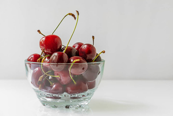 sweet cherries in a glass bowl on a light glossy surface with copy space - Zdjęcie, obraz