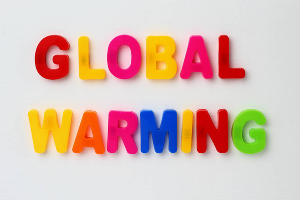Text made in multicolored magnetic letters. GLOBAL WARMING. White wooden background. - Foto, imagen