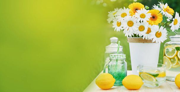 Limonade en madeliefjes bloemen op tafel. Mason potje limonade met citroenen. Gezellige ochtend. Voorjaars- en zomerseizoenskaart. Gezond eten en drinken. Zomervakantie. Een picknick buiten. Moederdagskaart. - Foto, afbeelding