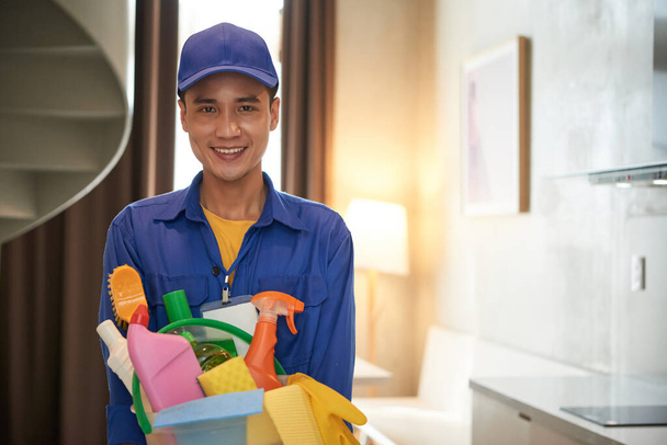 Портрет усміхненого працівника в "єтнамського прибирання, який тримає відро миючих засобів та дезинфікуючих розпилювачів. - Фото, зображення