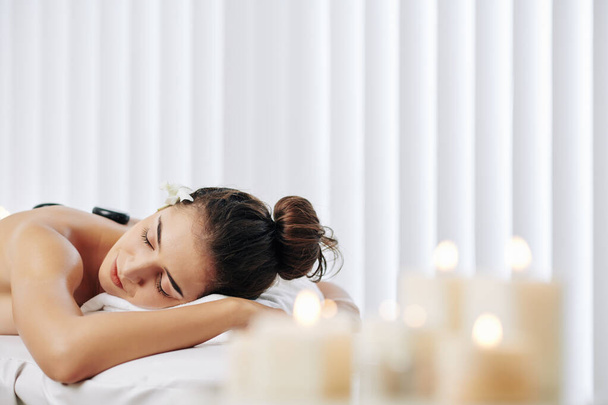 Pretty young woman fell asleep during procedure of stone massage in spa salon - Fotografie, Obrázek