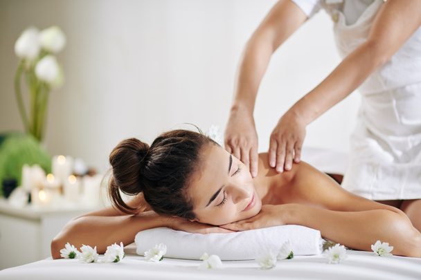 mooie jonge vrouw ontspannen op bed in spa salon en het krijgen van terug massage - Foto, afbeelding