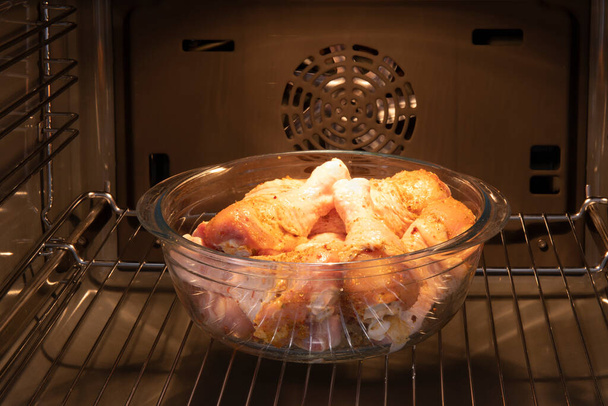 Fresh chicken legs in the oven before roasting - Foto, afbeelding