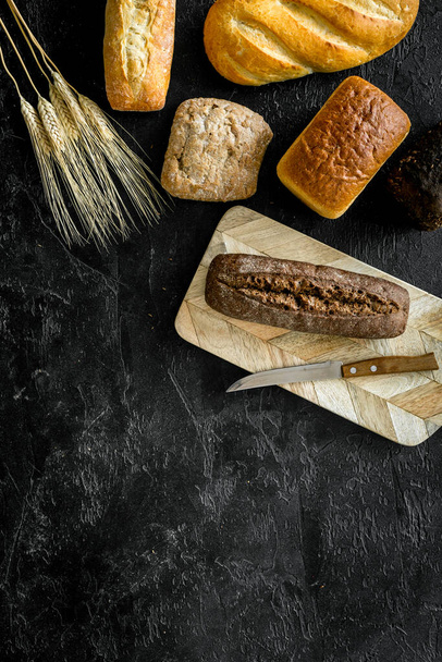 Homemade bread with wheat ear on dark kitchen desk. Top view - Фото, изображение