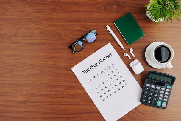 Calendario, calculadora, taza de café negro y auriculares en la mesa de la oficina, vista desde arriba
 - Foto, imagen