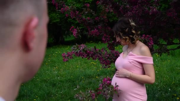 Чоловік дивиться на вагітну жінку, яка стоїть біля червоного дерева в парку
 - Кадри, відео