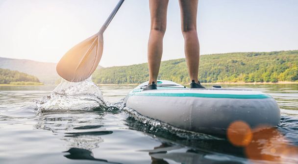 Levantarse paddle boarding en un lago tranquilo en verano, primer plano de las piernas
 - Foto, Imagen