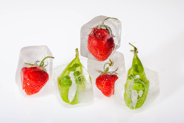 Fresh strawberries and peas frozen in ice cubes on white background closeup. Concept of freezing fruits. - Valokuva, kuva