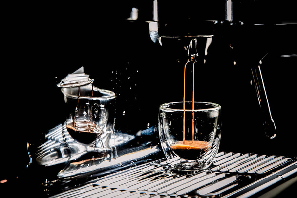 Donkere koffie in een doorzichtige glazen espressobeker van een handmatig espressomachine, met kopieerruimte, close-up - Foto, afbeelding