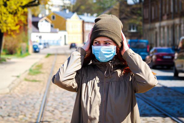 Красивая молодая европейская женщина с рыжими волосами на улице в медицинской маске на лице
 - Фото, изображение