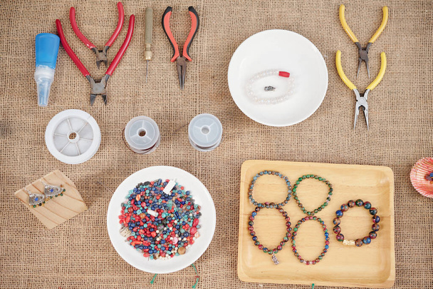 Alicates, cortadores de alambre, perlas y bandeja con pulseras de piedras preciosas hechas a mano en la mesa
 - Foto, Imagen