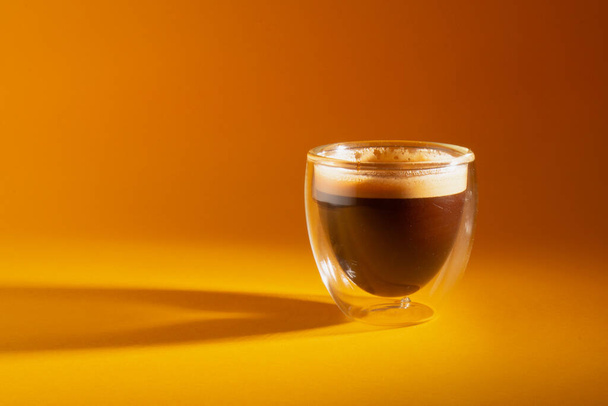 Frisch gebrühter cremiger Espresso in einer Glaskaffeetasse isoliert auf gelbem Hintergrund, Nahaufnahme mit Kopierraum - Foto, Bild