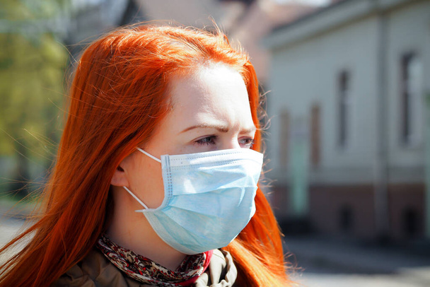 Красивая молодая европейская женщина с рыжими волосами на улице в медицинской маске на лице
 - Фото, изображение