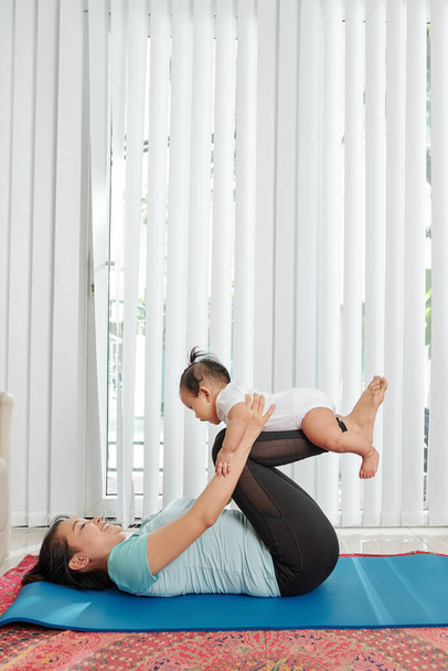 Aktive junge Mutter trainiert und spielt mit ihrer kleinen Tochter zu Hause - Foto, Bild