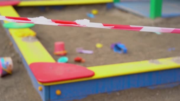 Κόκκινο και άσπρο οδόφραγμα προειδοποιούν φράχτες από αγνώστους από την είσοδο στην άδεια παιδική χαρά σε θολή φόντο των παιδιών εγκαταλειφθεί ξεχασμένα παιχνίδια σε αμμόλοφο στην άμμο. Κοίτα από κοντά. Εξωτερική. - Πλάνα, βίντεο