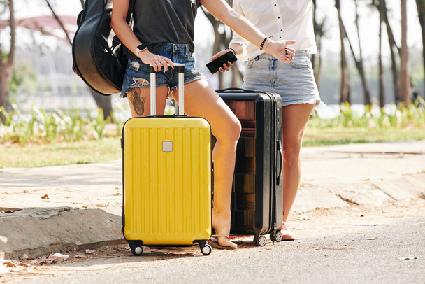 若い女性のトリミングされたイメージでデニムショートパンツは高速道路に立ってスーツケースとキャッチ車 - 写真・画像