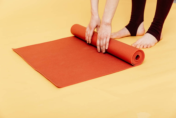Крупный план привлекательной молодой женщины складывая красную йогу или фитнес коврик после тренировки на желтом фоне. Йога и концепция здорового образа жизни. Горизонтальный выстрел. Снимок студии
 - Фото, изображение