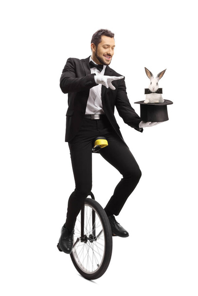 Magician riding a unicycle and performing a hat-trick with a rabbit isolated on white background - Zdjęcie, obraz
