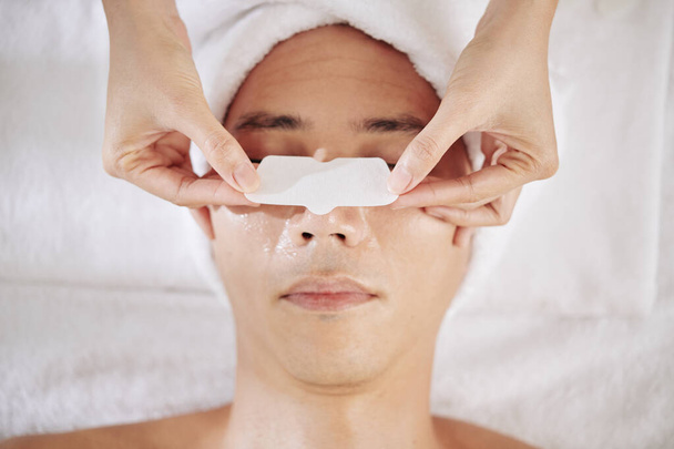 Косметолог наносит полоску носа на нос молодого человека, чтобы очистить поры
 - Фото, изображение