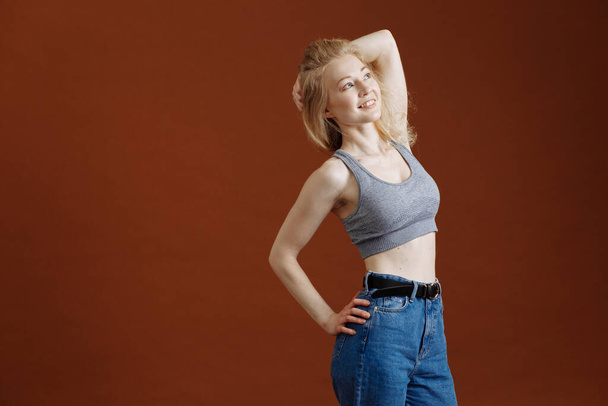 emotions, people, beauty and lifestyle concept - Portrait of fashionable young girl, a cgray crop top and jeans over brown background, copyspace. Vogue style. Studio shot. model tests - Фото, изображение