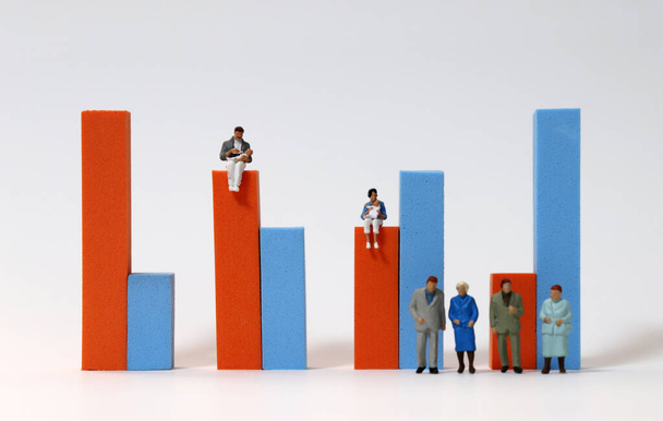 Miniature people standing in front of a bar graph and Miniature people sitting on a bar graph. - Photo, Image