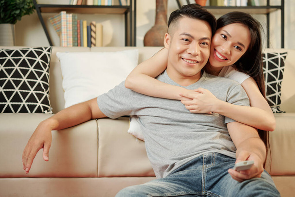 Beautiful young Vietnamese woman hugging her boyfriend while watching game on tv at home - Fotografie, Obrázek