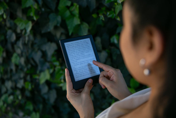 ラテン系の若い女性がデジタルタブレット端末で本を読んでいます。電子ブックに焦点を当てる. - 写真・画像